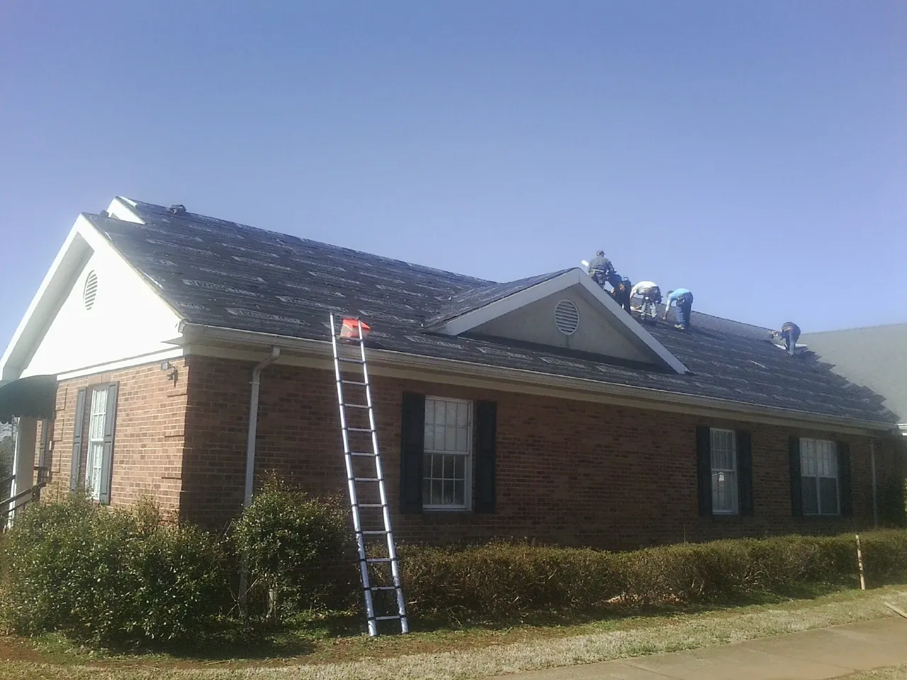 Crew tearing shingles off a brick ranch roof with a ladder set — Emergency Roof Repair work by our crew in Scott