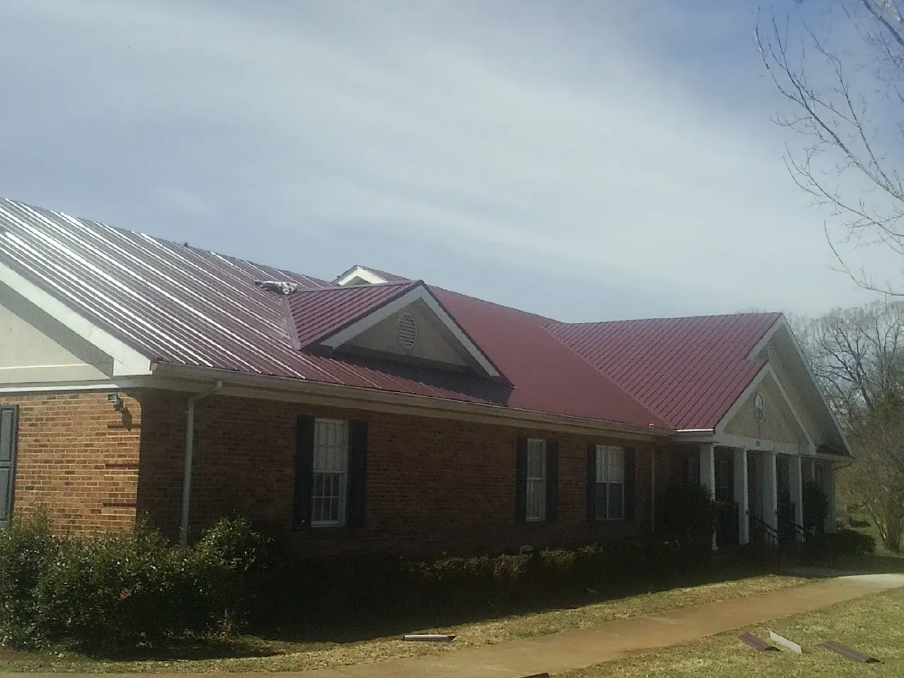 Red metal roof with gabled entries on a long brick building, from a Hail Damage Roof Repair job in Scott