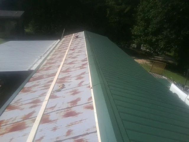 Old rusted panels beside newly installed green metal roofing — Wind Damage Roof Repair by Roofing Brothers in Scott