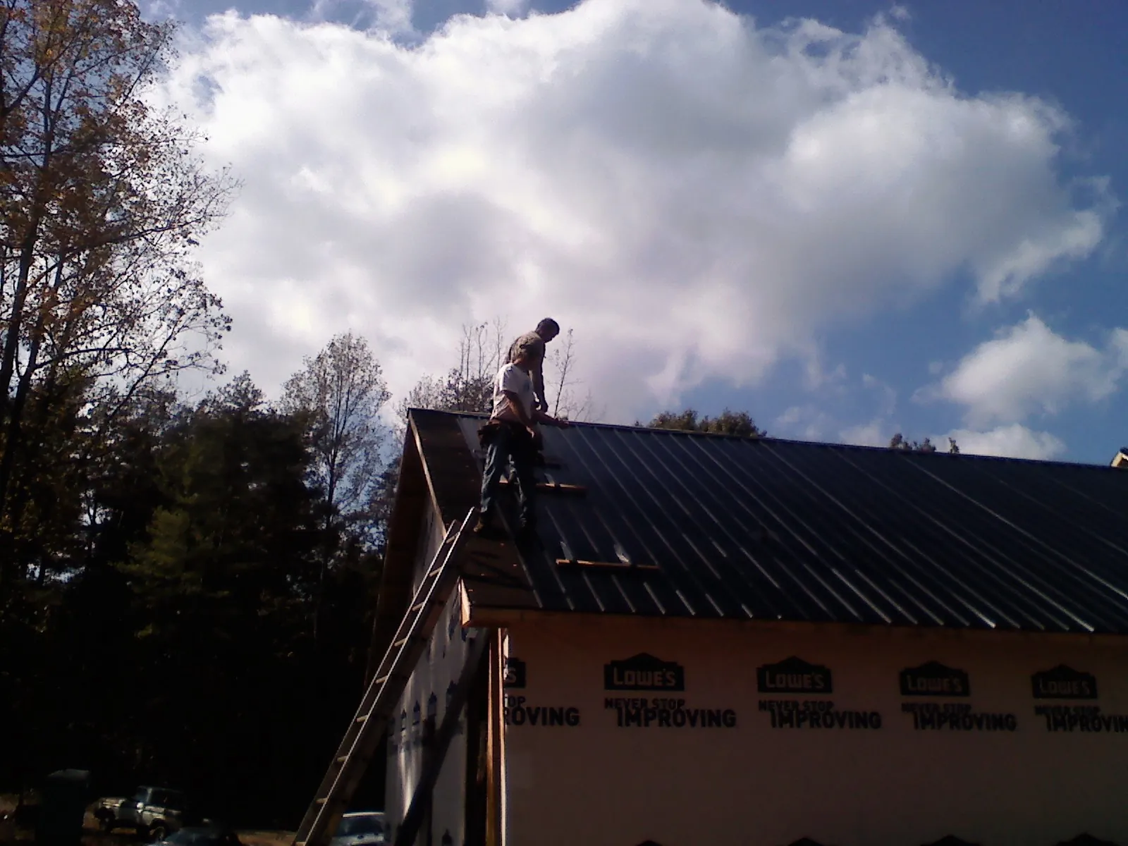 Roofer fastening dark metal panels high against a cloudy sky, from a Roof Inspection job in Scott