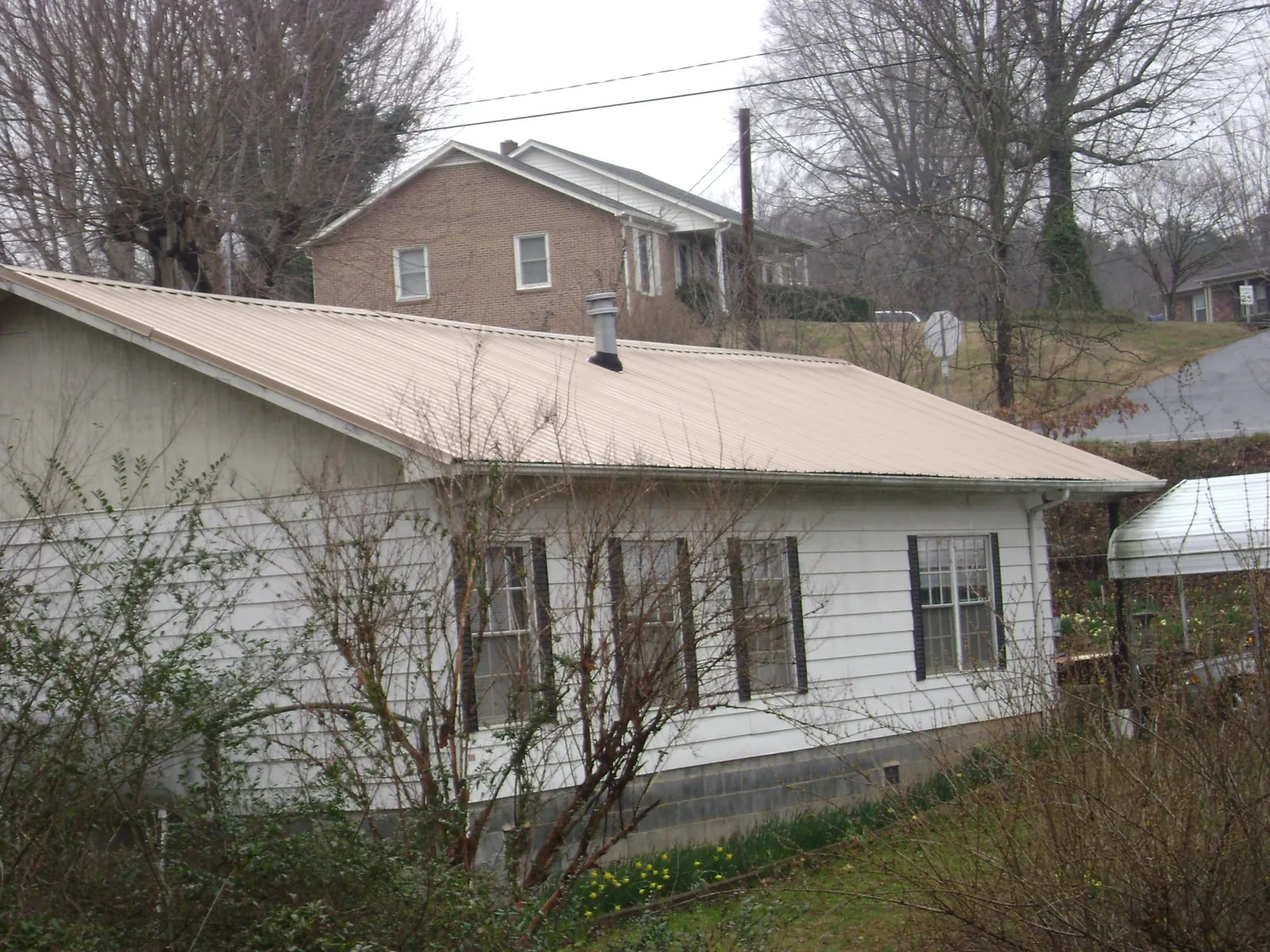 Tan metal roof on a white sided house set into a hillside — Commercial Roofing by Roofing Brothers in Scott