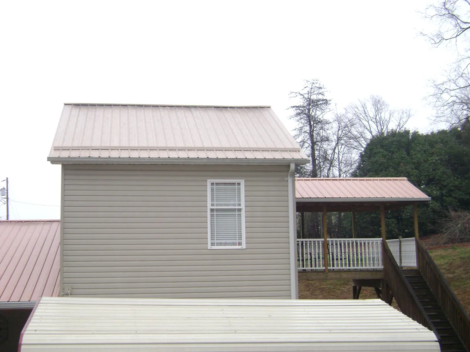 Tan metal roofs on a two story addition and attached porch, from a Roof Replacement job in Scott